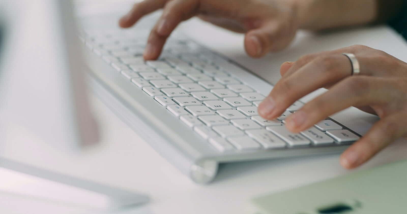 Handen typen op een toetsenbord aan een lichte werkplek - digitale gegevensverwerking onder NEN7510-informatiebeveiliging
