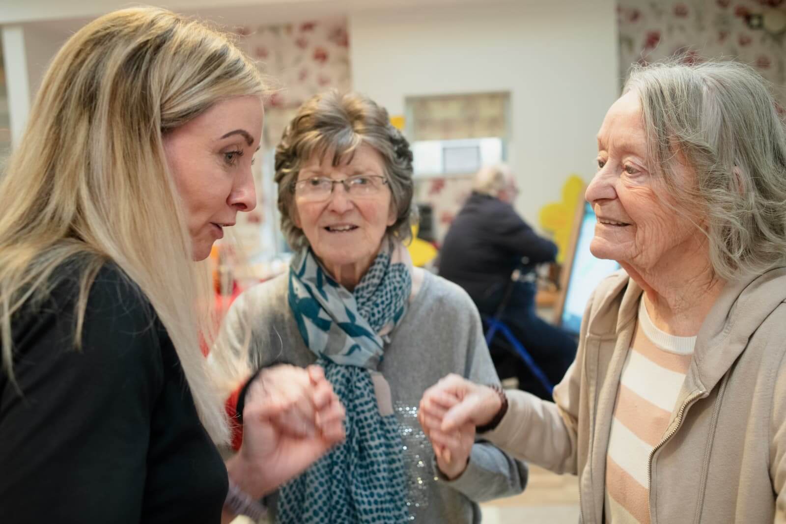 Zorgmedewerker in geanimeerd gesprek met twee oudere cliënten in een woonruimte - WLZ-zorg in huiselijke setting